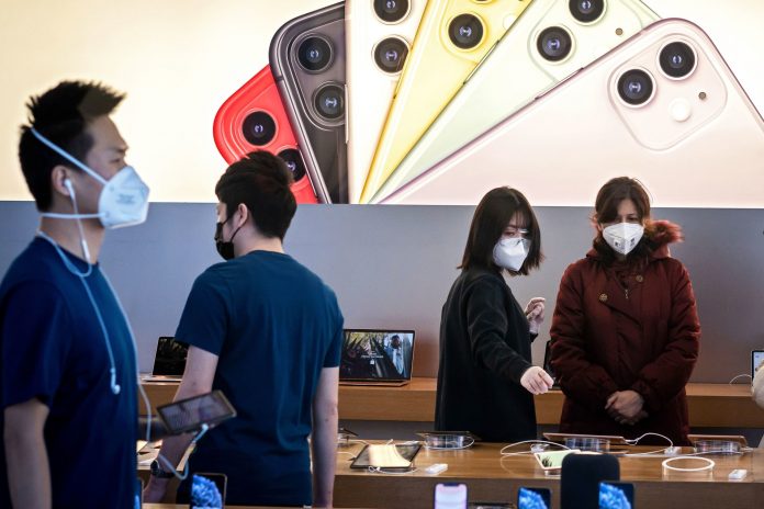 Apple staff and customers, wearing facemasks to protect against the COVID-19 coronavirus, are seen on the shop premises in Beijing on February 22, 2020.