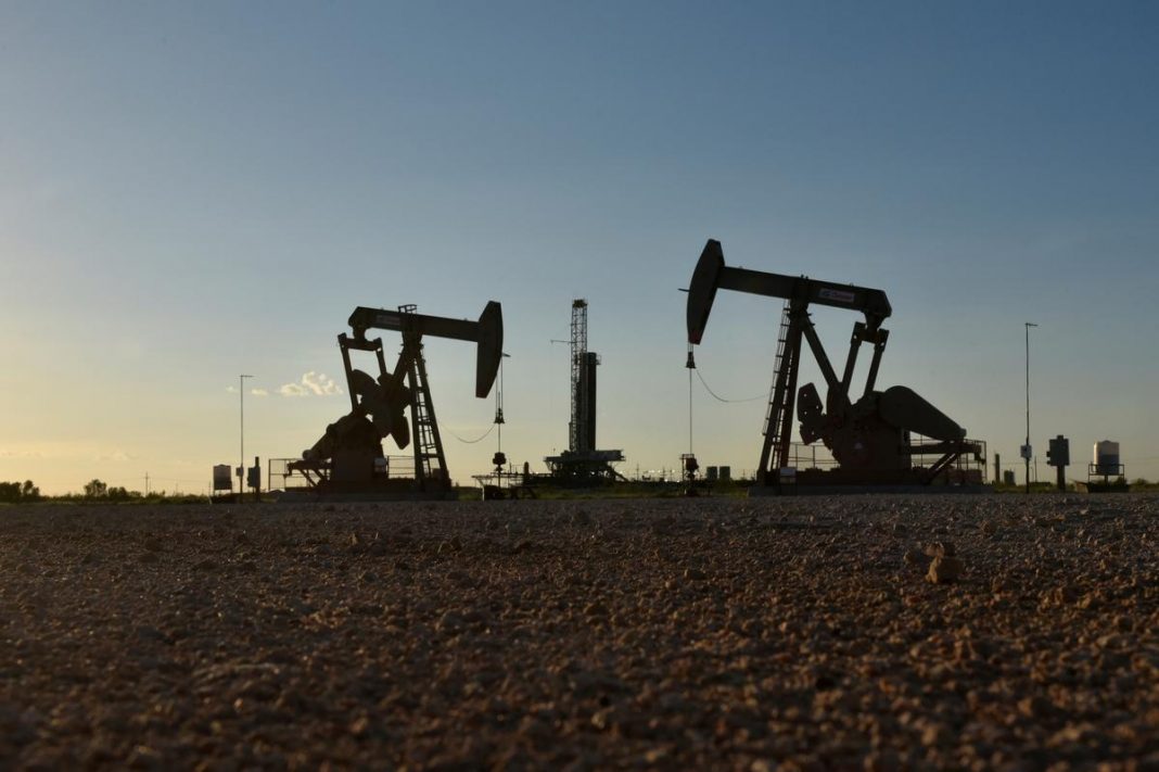 Pump jacks operate in front of a drilling rig in an oil field in Midland, Texas U.S.