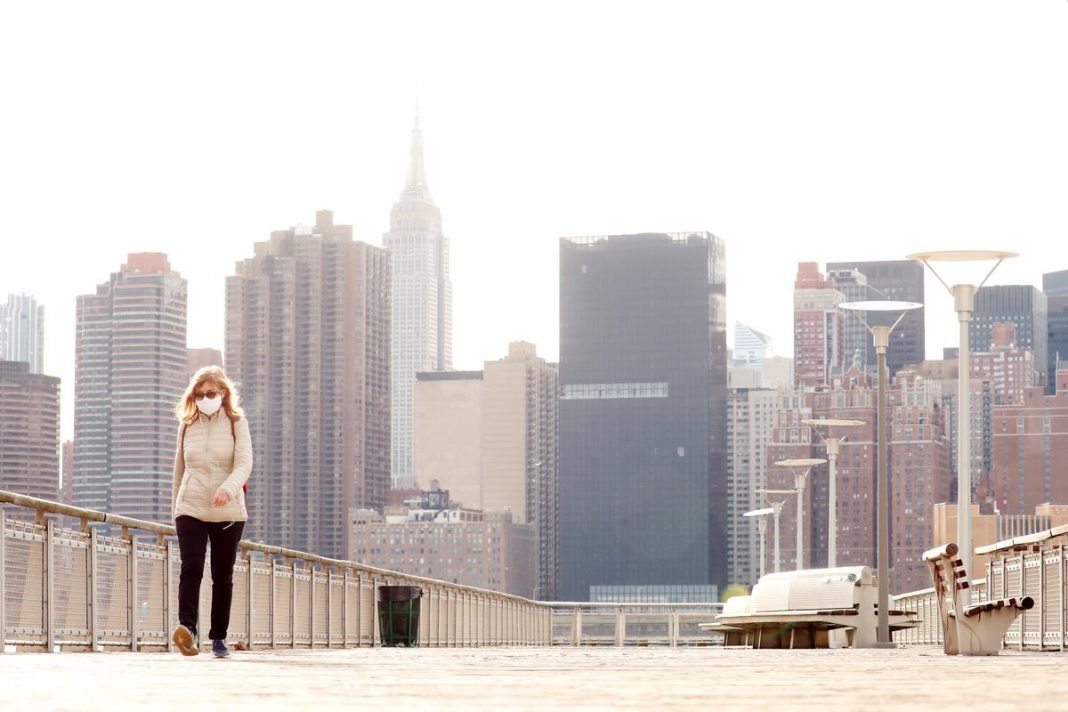 Pedestrians walk through a park, with the skyline of Manhattan rising behind them, amid the coronavirus disease (COVID-19) outbreak, in the Queens borough of New York City, U.S.
