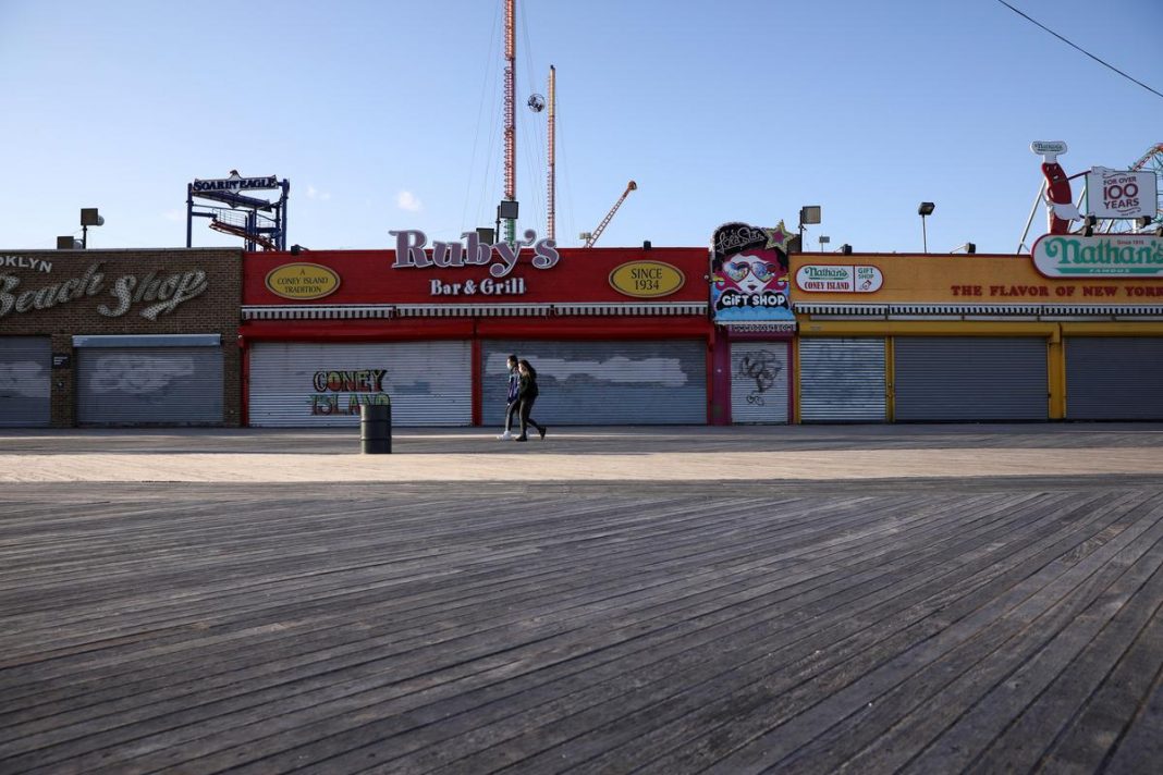 People wearing protective masks walk past closed shops on the the Coney Island boardwalk during the outbreak of coronavirus disease (COVID-19) in Brooklyn, New York, U.S.