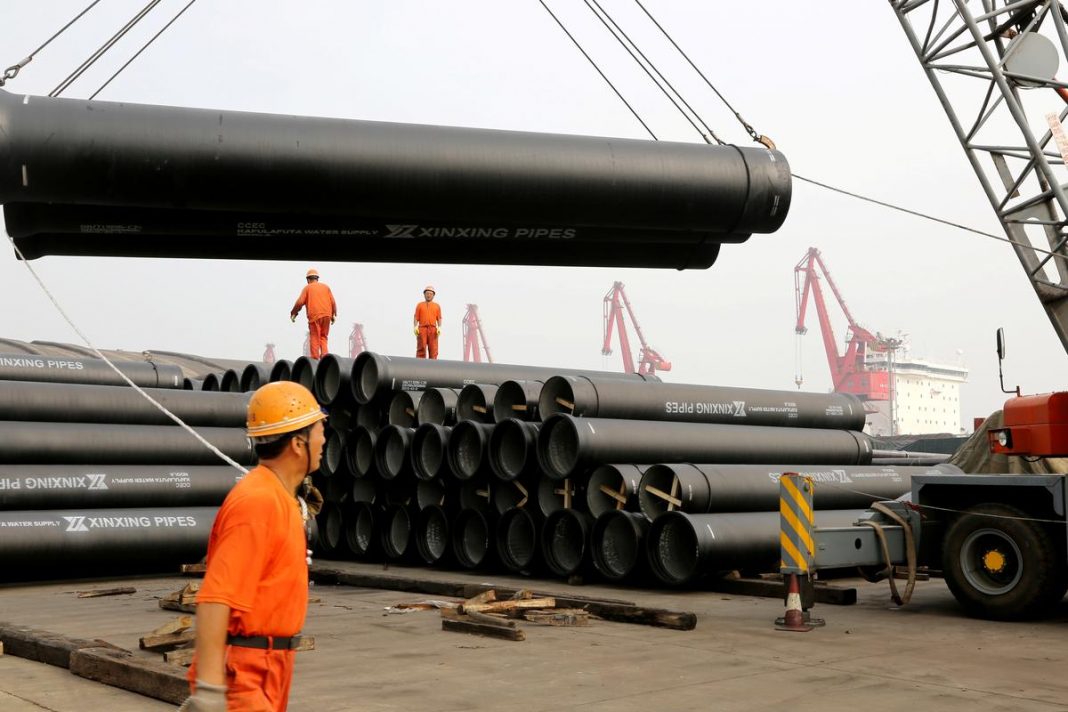 Workers direct a crane lifting ductile iron pipes for export at a port in Lianyungang, Jiangsu province, China June