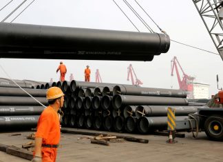 Workers direct a crane lifting ductile iron pipes for export at a port in Lianyungang, Jiangsu province, China June